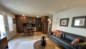 Un salon moderne avec un canapé en cuir foncé, une table basse ronde et un coin repas comprenant des chaises et une table en bois.