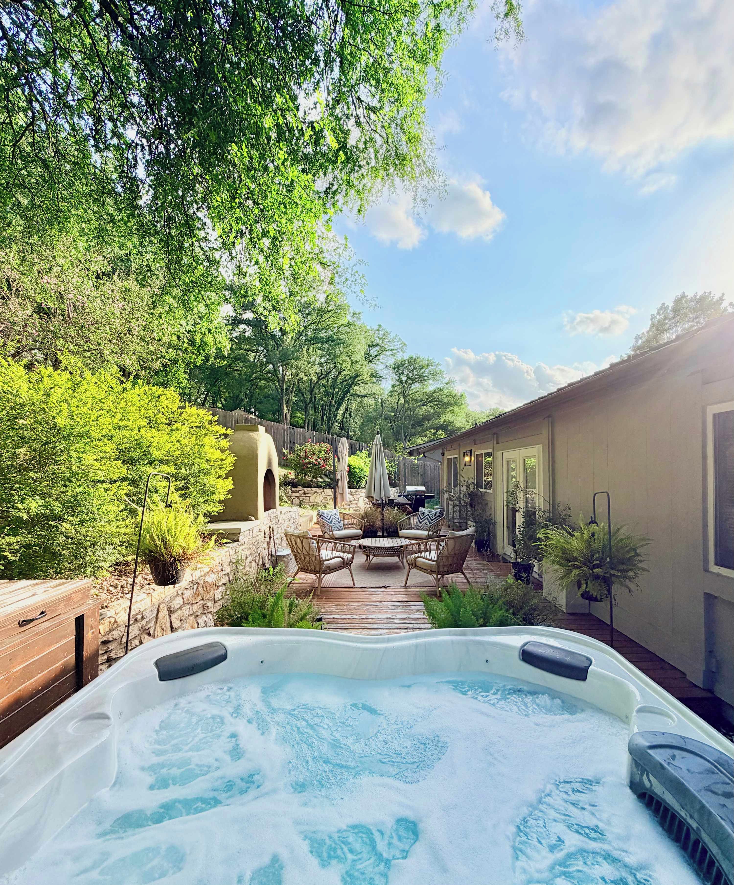 A hot tub surrounded by a wooden deck, stone walls, and lush greenery.