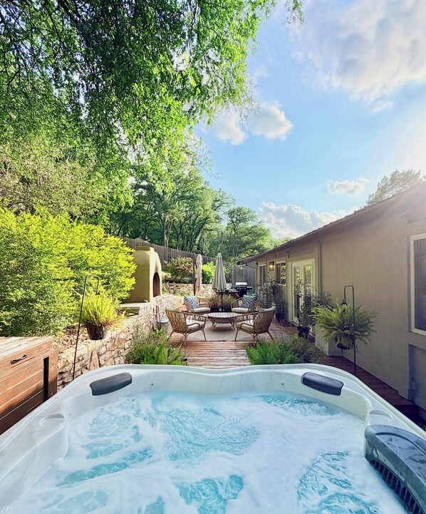 A hot tub surrounded by a wooden deck, stone walls, and lush greenery.