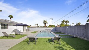Un giardino sul retro con piscina, prato sintetico e poltrone relax.