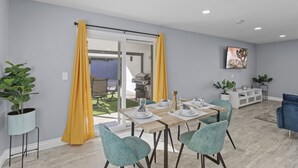 Zona pranzo con tavolo apparecchiato per quattro persone, una porta scorrevole in vetro che dà su un patio esterno e una TV a parete.