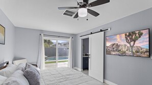 Una camera da letto con un letto, una ventola a soffitto, una porta scorrevole su un patio e un quadro raffigurante un paesaggio desertico.