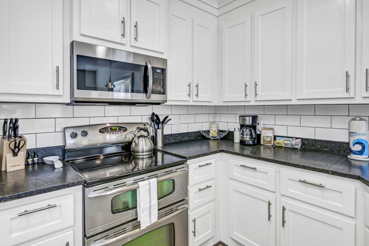 A modern kitchen with white cabinets, stainless steel appliances, and a black countertop.