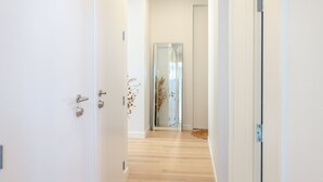 A hallway with a wooden floor, white walls, and a glass elevator. - Wavesong Whakaaio Onetangi | Be My Guest (Waiheke Island)