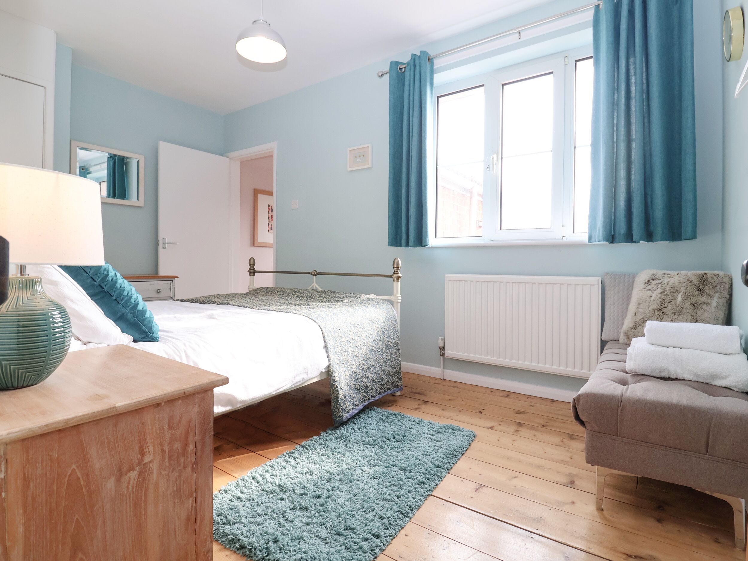 A bedroom with a bed, bedside table, lamp, and a window with curtains.