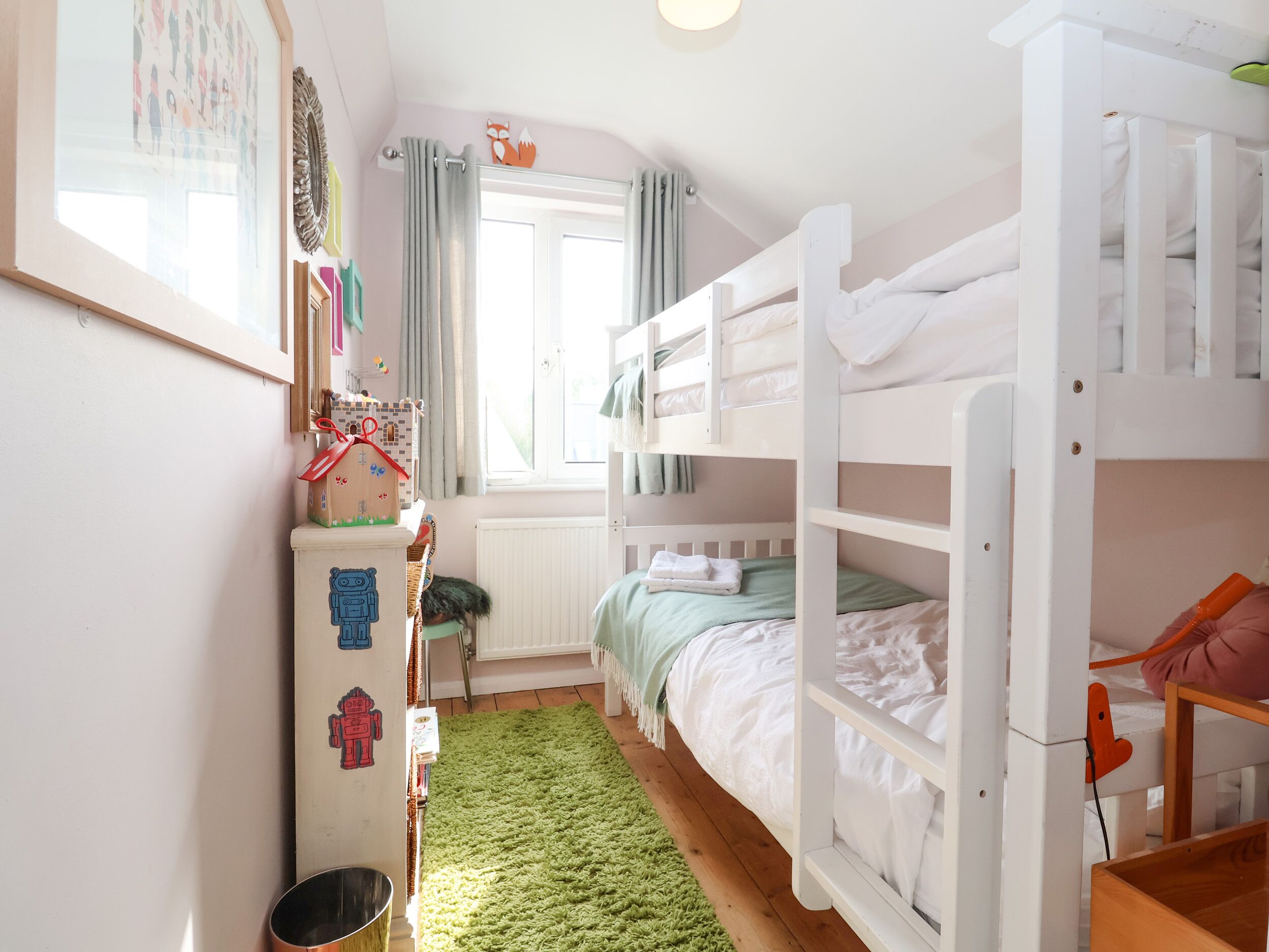 A child's bedroom with bunk beds, a dresser, a radiator, and a window with curtains.