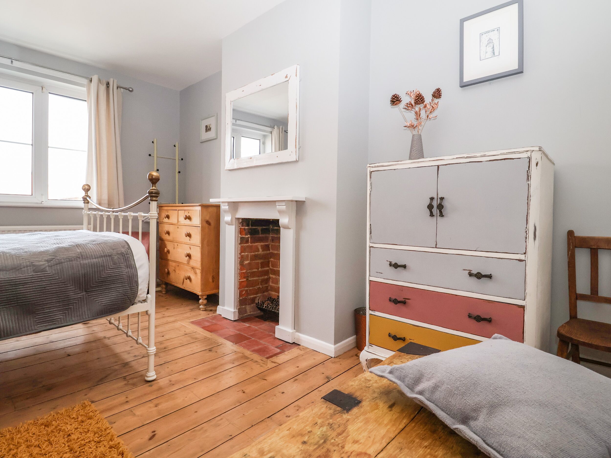 A bedroom with a bed, dresser, mirror, fireplace, and a window with curtains.