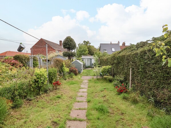 Un sendero conduce a una casa rodeada de abundante vegetación y un jardín.