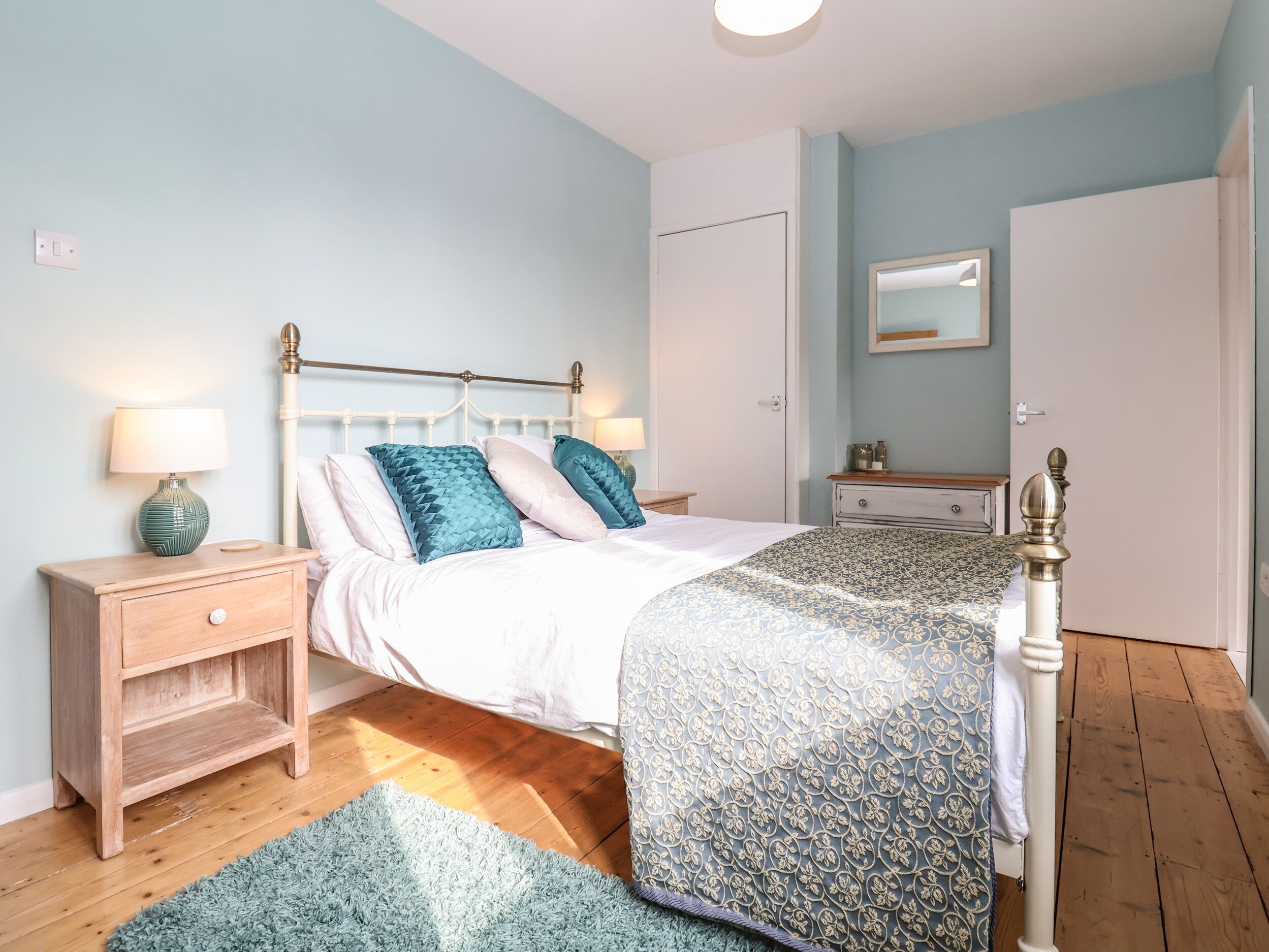 A bedroom with a bed, nightstands, a dresser, a mirror, and a door.