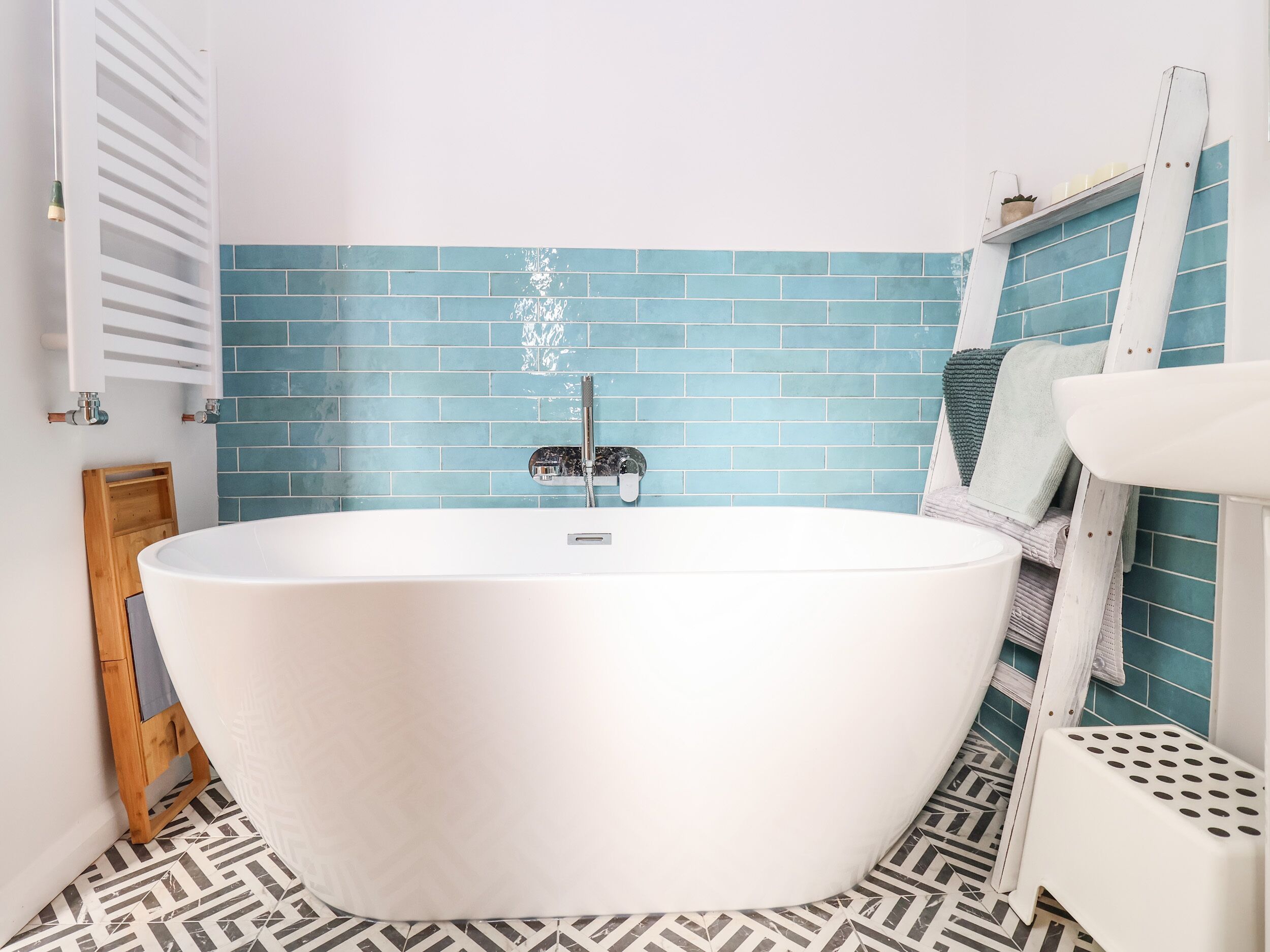 Ein modernes Badezimmer mit freistehender Badewanne, blauen Fliesenwänden und einem gemusterten Boden.