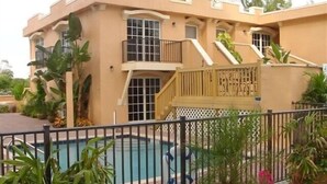 A two-story building with a swimming pool, surrounded by a fence and potted plants. - Villa-style condo with pool on the beach - Condo 1 (Holmes Beach)