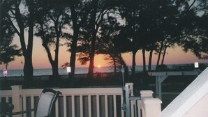 A balcony with a view of the sunset over the ocean, surrounded by trees. - Villa-style condo with pool on the beach - Condo 1 (Holmes Beach)