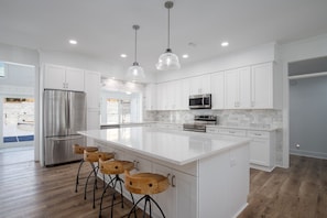 Une cuisine moderne avec des meubles blancs, des appareils en acier inoxydable et un grand îlot central doté de tabourets de bar.