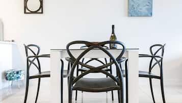 A dining area with a white table and four chairs with a crisscross design. A bottle of wine is on the table.