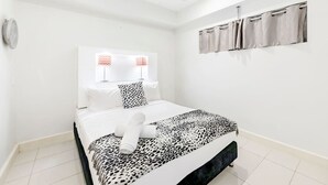 Een slaapkamer met een bed, een plafondventilator, een raam met gordijnen en een handdoekhouder aan de muur.