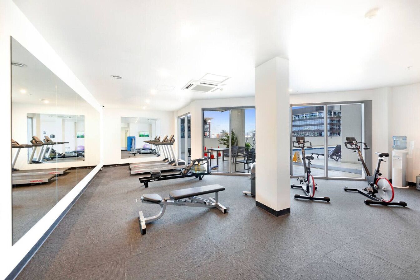 Une salle de sport moderne équipée de machines de cardio, de bancs et d’un grand miroir.