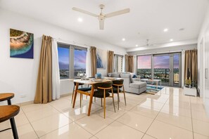 A modern living room with a dining area, large windows, and a city view. - Reef-side Splendor: City Vistas ~ Pool ~ Workspace (Darwin City)