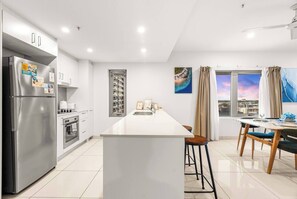 A modern kitchen with a central island, stainless steel appliances, and a dining area with a view. - Reef-side Splendor: City Vistas ~ Pool ~ Workspace (Darwin City)
