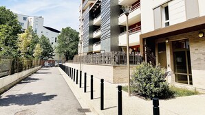 A modern urban street with multi-story buildings, a sidewalk, and a metal fence. - Bright, young private room (Saint-Denis)