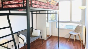A bunk bed with checkered bedding, a wicker chair, a lamp, and a view of the outside through a window. - Bright, young private room (Saint-Denis)