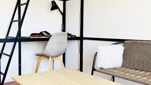 A room with a wooden table, a grey office chair, a wicker sofa, and a black ladder against the wall. - Bright, young private room (Saint-Denis)