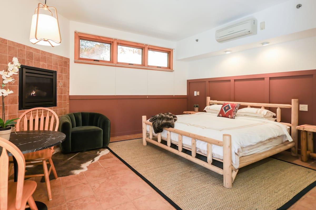 Ein Schlafzimmer mit einem hölzernen Bett, einem kleinen Tisch, einem Sessel, einer Topfpflanze und einem Kamin.