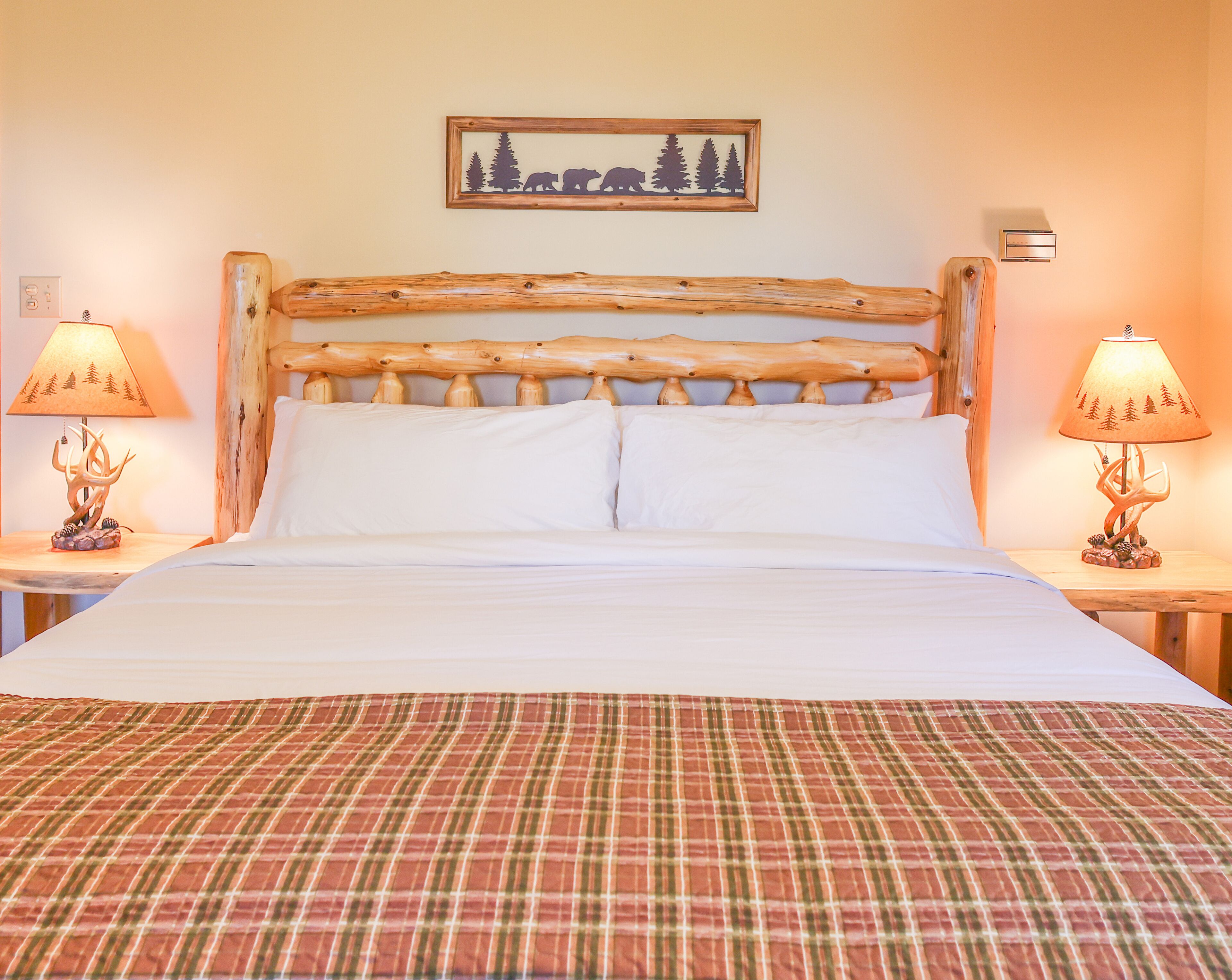 A bed with a plaid bedspread, a wooden headboard, and two bedside lamps.