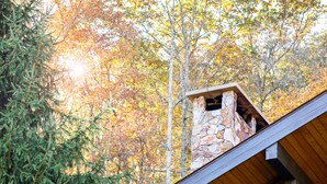 A cabin with a stone chimney, wooden deck, and surrounding trees.