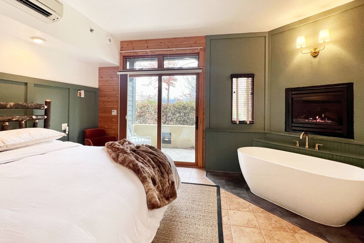 Ein Schlafzimmer mit einem großen Bett, einer Badewanne und einer Glasschiebetür, die auf einen Balkon führt.