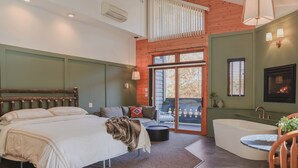 A bedroom with a large bed, a sitting area with a sofa, a bathtub, and a fireplace.