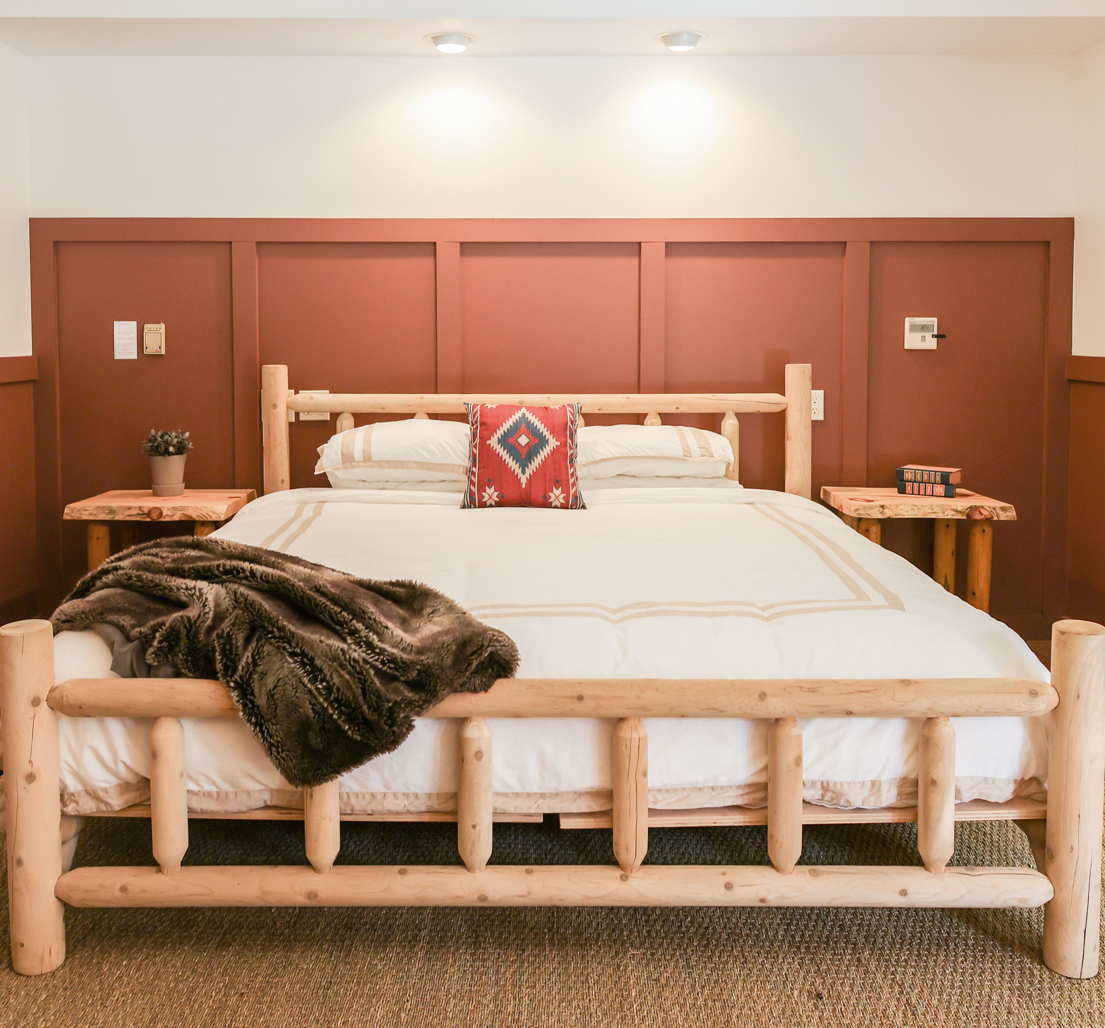 A wooden bed with a headboard, white bedding, and a throw blanket. There are two bedside tables with a plant and books on one.