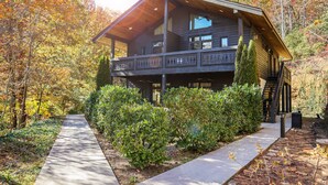 A two-story log cabin with a balcony, surrounded by autumn foliage.