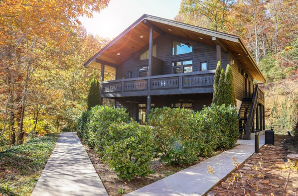 A two-story log cabin with a balcony, surrounded by autumn foliage. - Outland Chalet & Suites Great Smoky Mountains (Whittier)