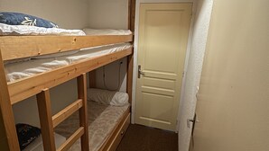 A narrow room with a bunk bed, a door, and a ceiling light fixture.