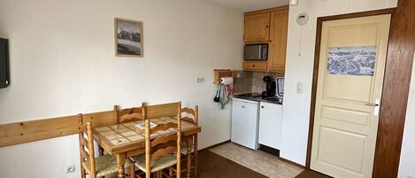 A compact room with a dining table and chairs, a kitchenette, a bed, and a door with a picture.