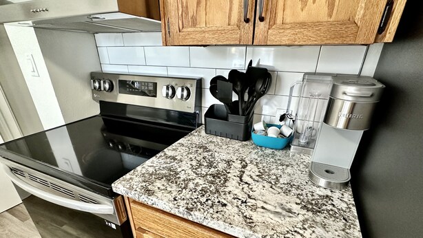 Una cocina con estufa de acero inoxidable, horno empotrado, gabinetes de madera, encimera de granito y cafetera.