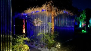 A water feature with a wooden structure and illuminated panels, surrounded by tropical plants and a pathway. - Exotic waterfront Glamping experience  (Port Charlotte)