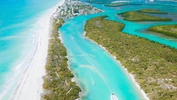An aerial view of a coastal area with a long stretch of sandy beach, clear turquoise waters, and a dense line of vegetation along the shore. - Exotic waterfront Glamping experience  (Port Charlotte)