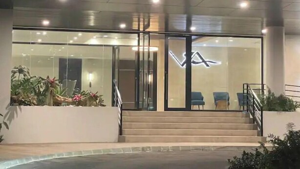 A modern building with a glass facade, a staircase leading to the entrance, and a logo with the letters "VA" illuminated on the wall.