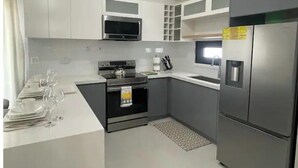 A compact kitchen with white cabinets, a built-in microwave, a stainless steel refrigerator, and a small countertop with a kettle and a coffee maker.