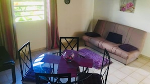 A living room with a round glass table, a sofa, and a small clock on the wall. - Gîte Papaye · RESIDENCE LES KALBASSIERS (Lamentin)