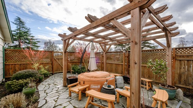 A wooden pergola with a hot tub, stone patio, and outdoor furniture. - Cozy Home in the Heart of Corvallis (Corvallis)
