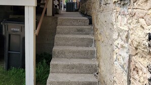A narrow alleyway with a concrete staircase leading up to a building. A sign on the wall indicates the direction to Raven's Nest on Top Floor.