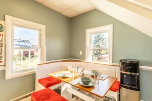 A dining area with a wooden table set for four, white cushioned benches, and a water dispenser.
