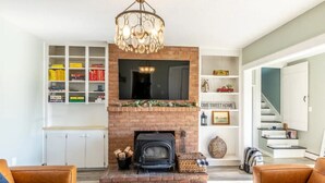 Una sala de estar con chimenea, un televisor montado encima y una estantería llena de libros.