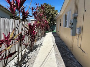 A narrow concrete pathway flanked by a wooden fence and a building with outdoor electrical boxes.