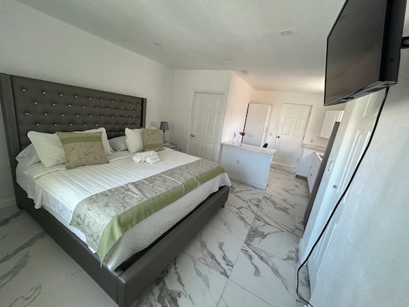 A bedroom with a large bed, a bedside table with a lamp, a small desk, and a television mounted on the wall.