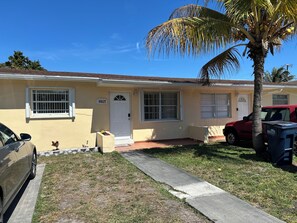 A residential building with a number 9017 sign, a front door, windows, a palm tree, and a parked car.