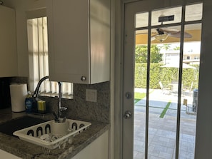 A kitchen with a sink, countertop, and cabinets. There is a door leading to an outdoor area with a patio.