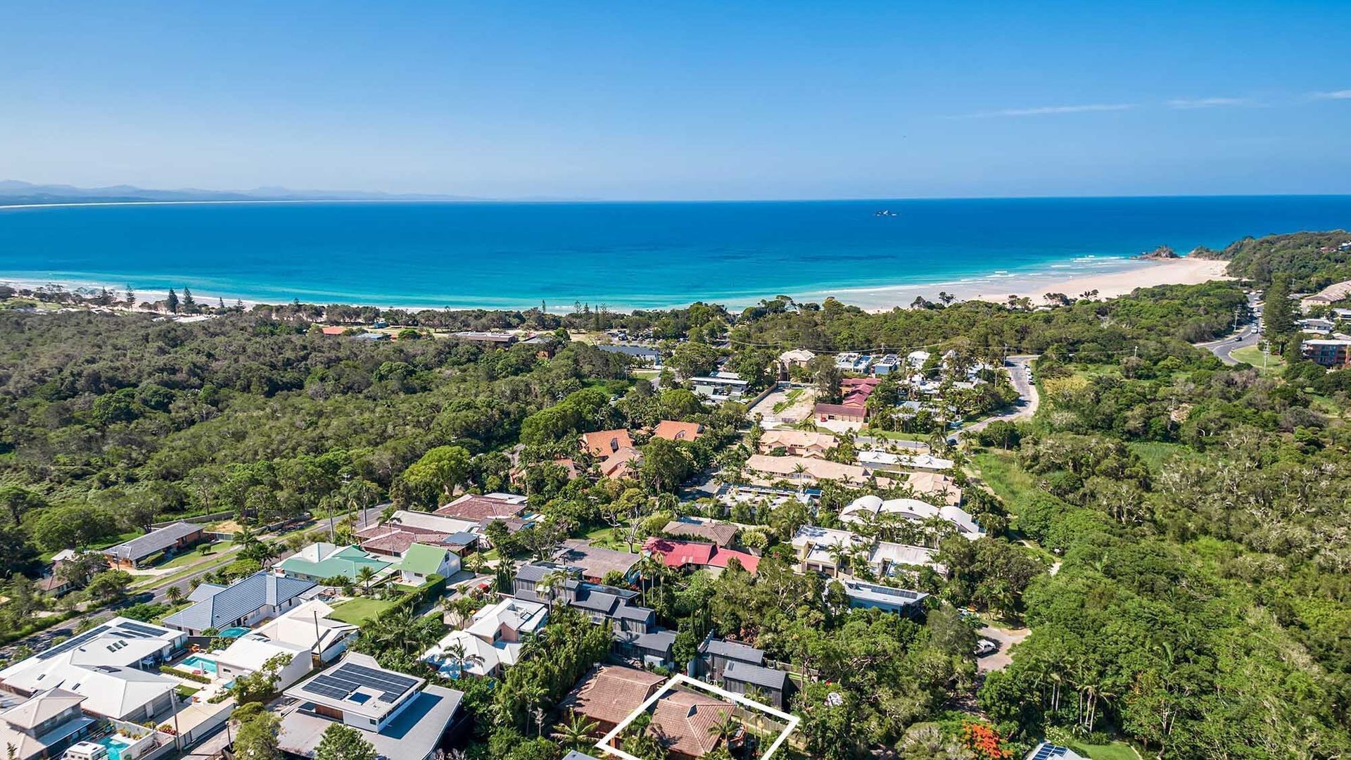 Vista aérea de uma área residencial costeira com casas, uma praia e um céu azul e límpido.